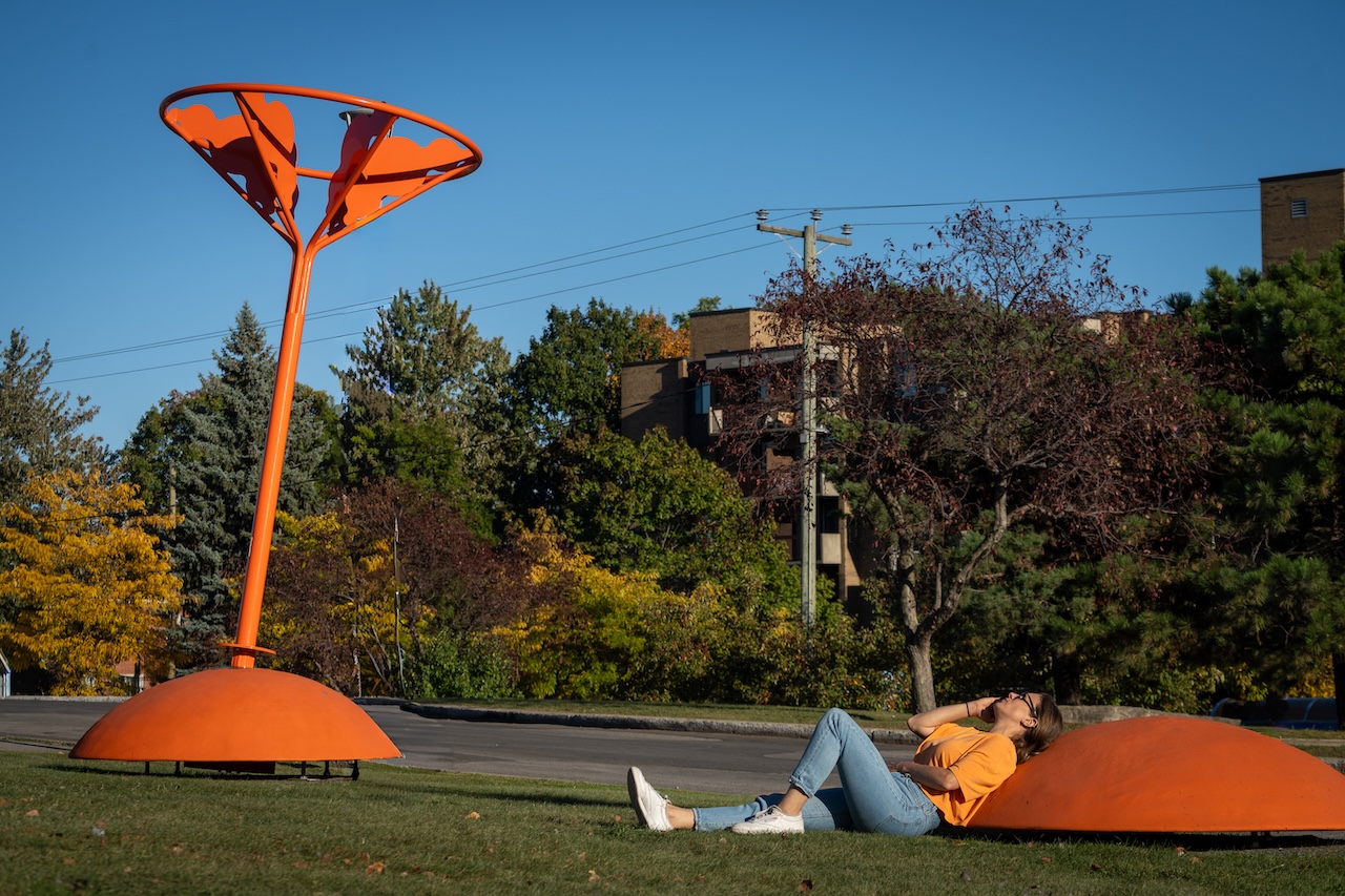 Installation artistique orange en plein air, avec une personne détendue à ses côtés.