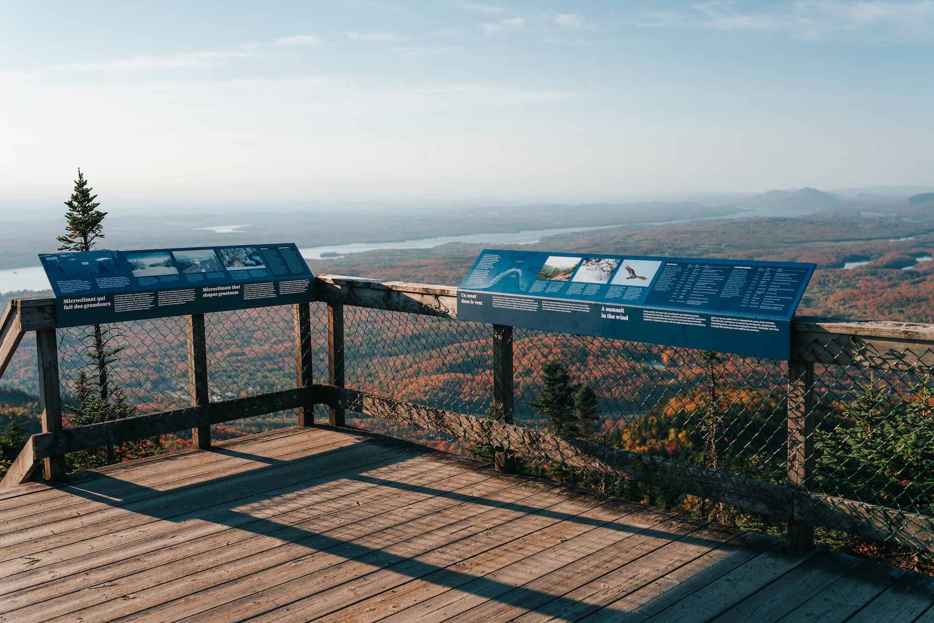 Vue panoramique depuis un point de vue en bois avec panneaux d'information sur un paysage automnal.
