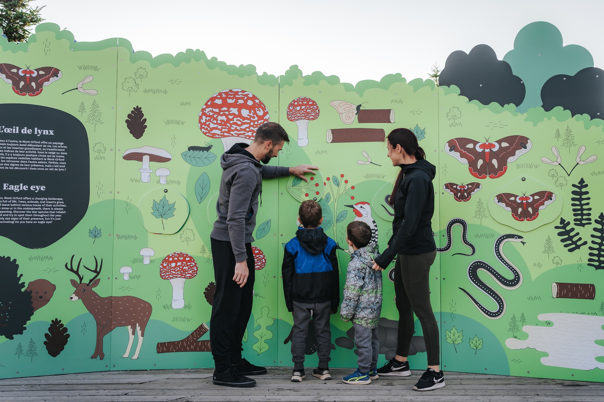 Famille découvrant une installation éducative forestière colorée de Studio Overall.