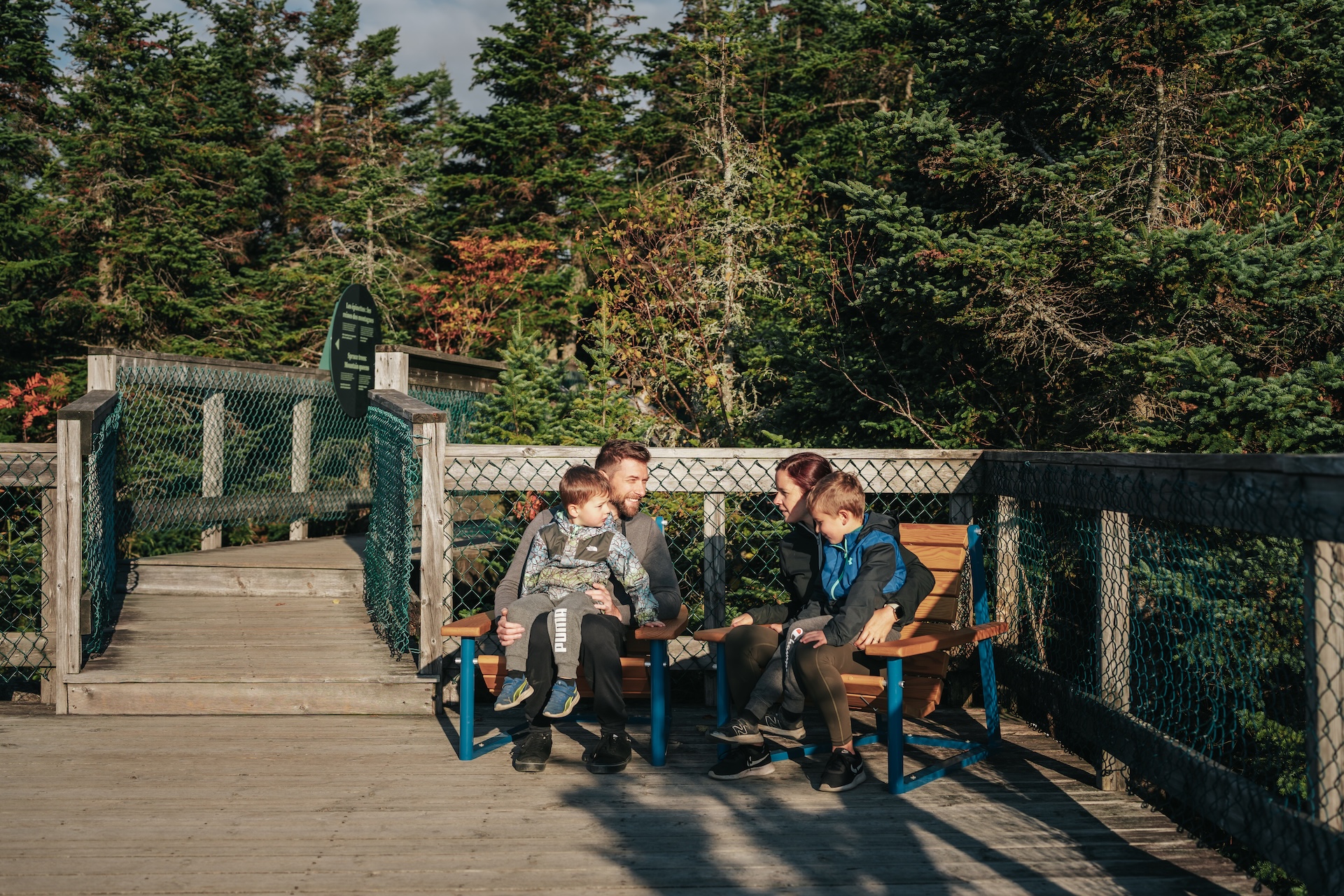 Famille assise sur un pont en bois dans un parc forestier, profitant du soleil.
