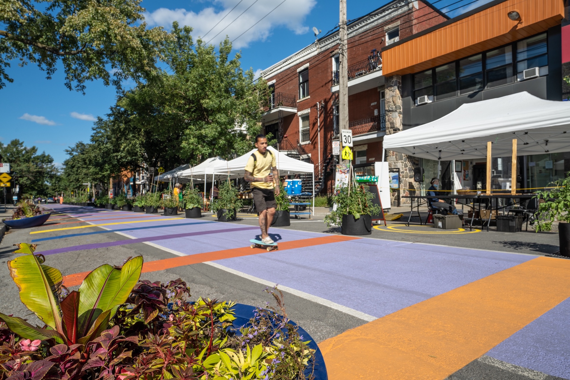 Rue colorée avec installations artistiques, marché de rue et passant en planche à roulettes.