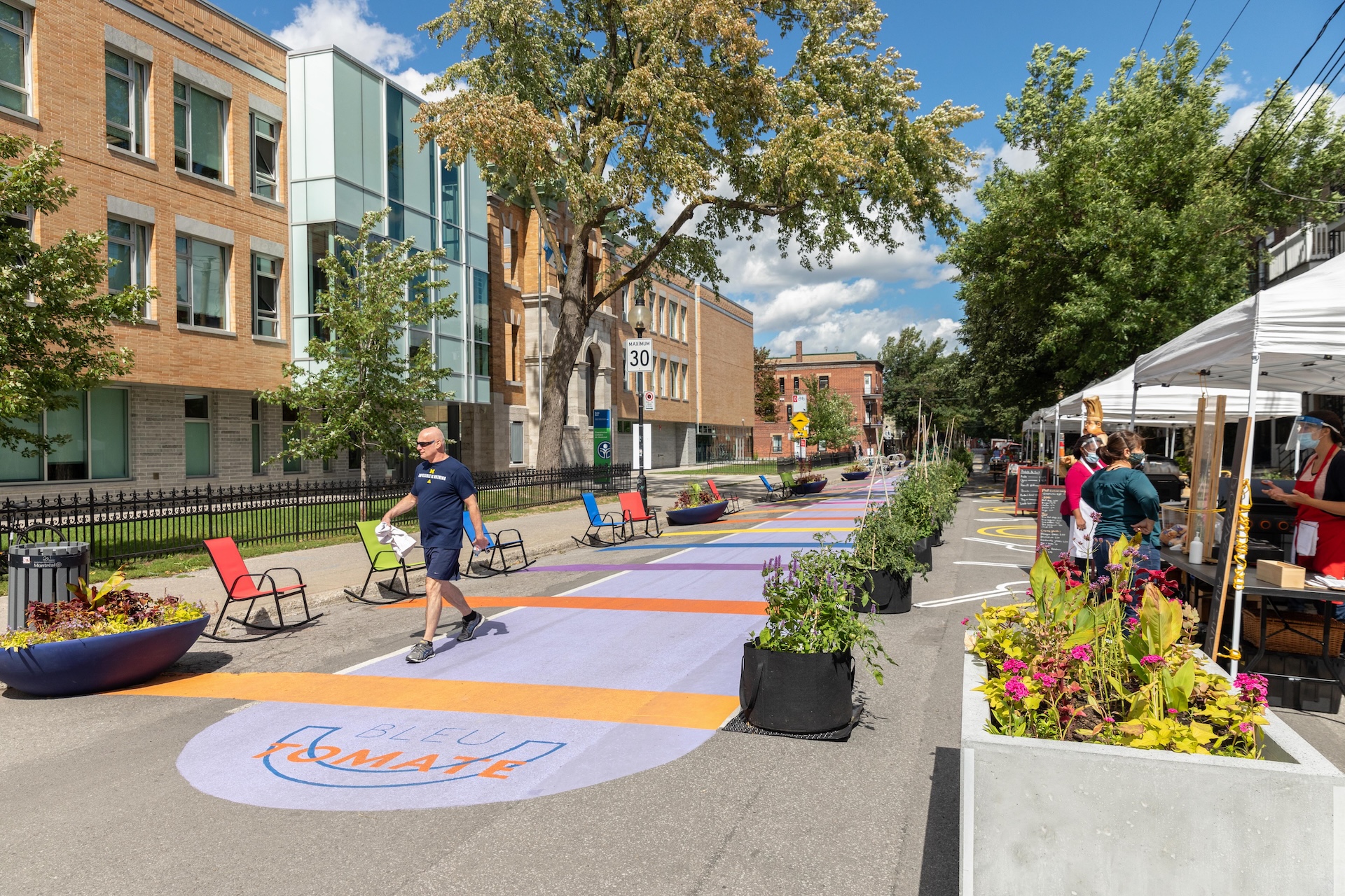 Rue colorée avec installations urbaines, plantes et personnes, œuvre de Studio Overall.