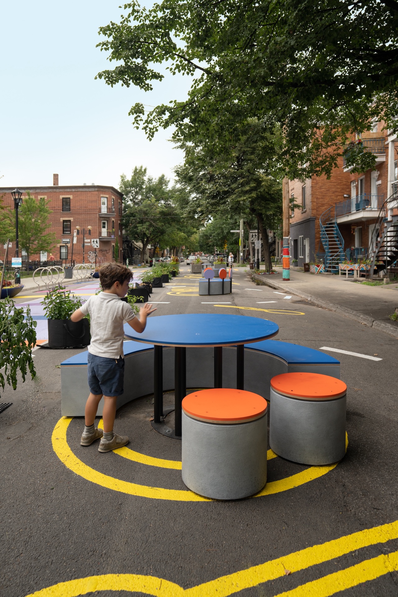 Installation urbaine colorée avec un enfant jouant autour d'une table et de tabourets.