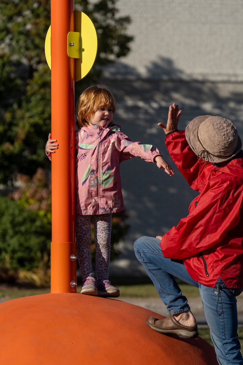 Enfant et adulte interagissent sur une structure de jeu orange en plein air.
