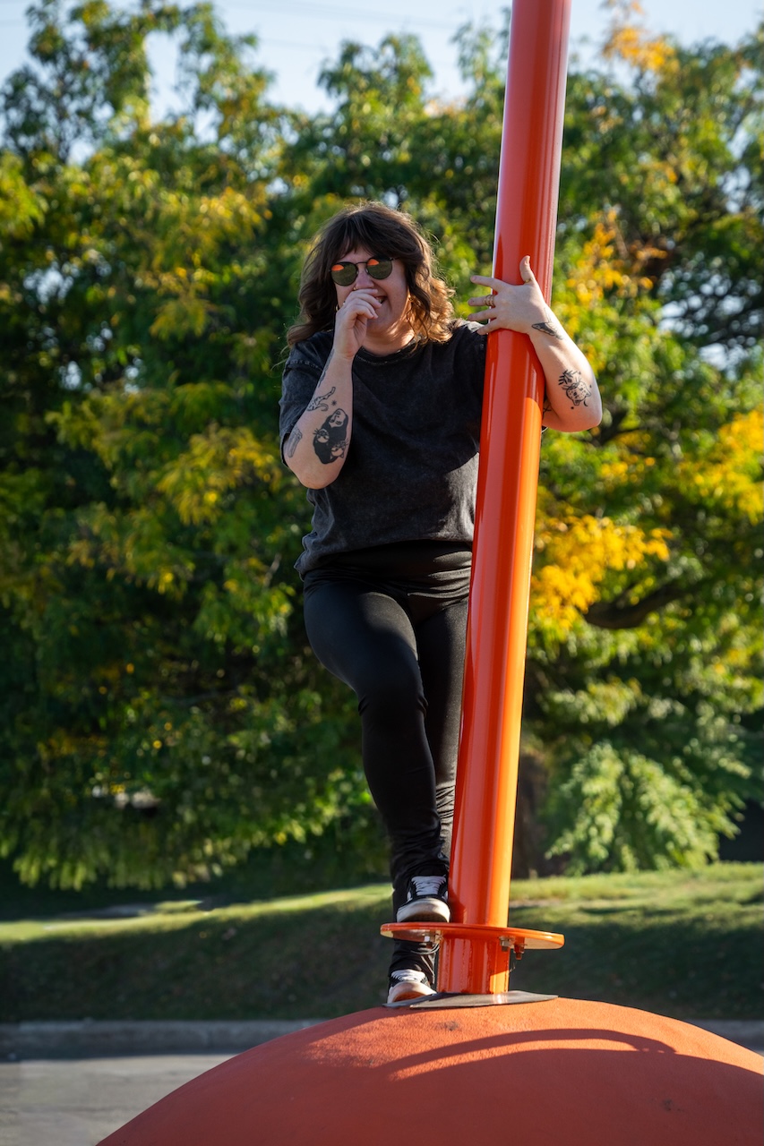 Personne grimpe sur une structure orange en plein air, arrière-plan verdoyant.