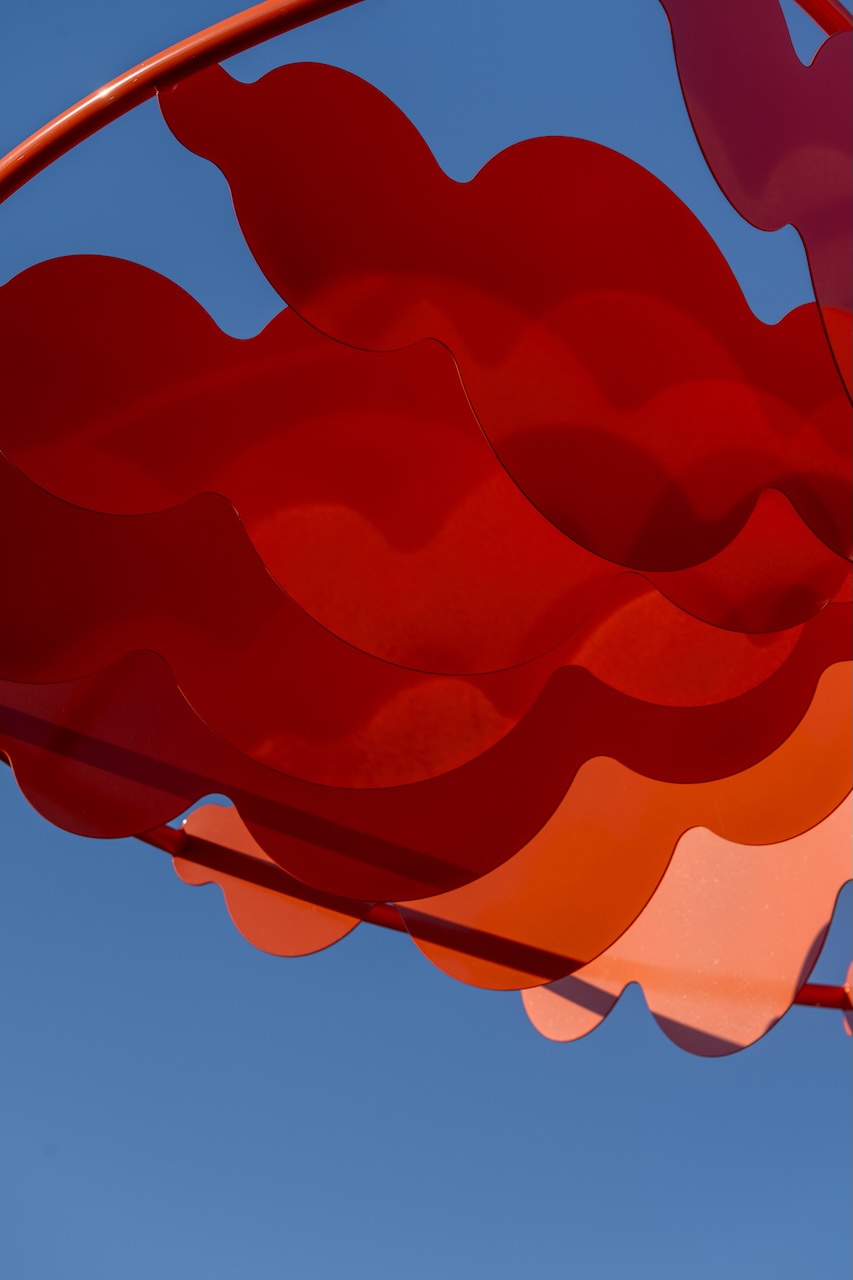 Installation artistique rouge ondulée contre un ciel bleu, œuvre de Studio Overall.
