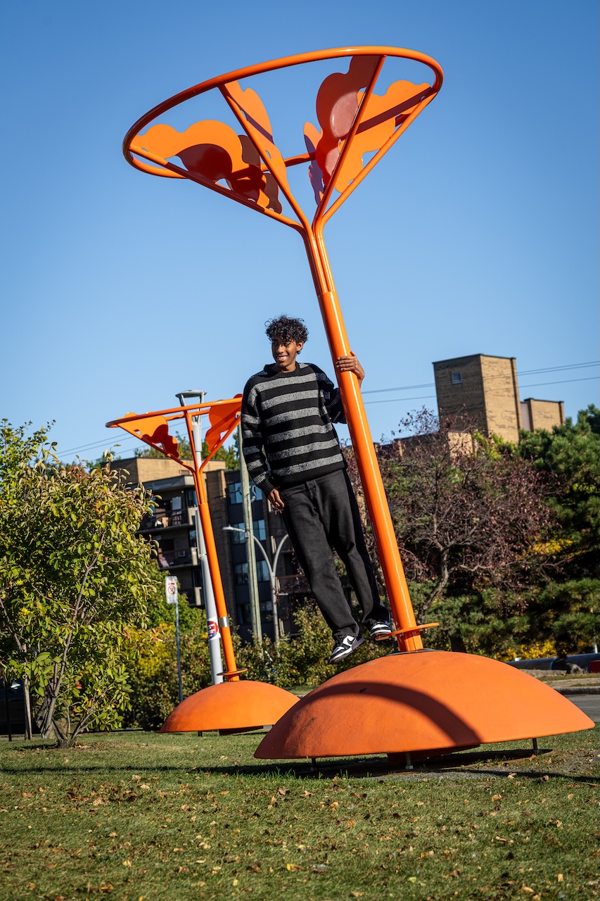 Installation artistique orange en plein air, avec une personne posant près d'une structure moderne.