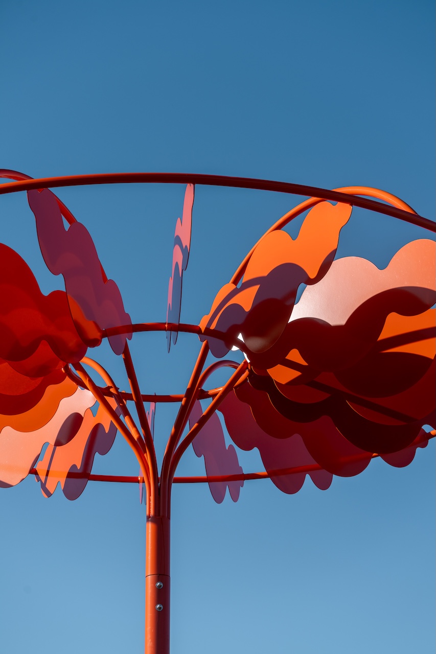 Installation artistique en métal rouge-orange contre un ciel bleu, œuvre de Studio Overall.