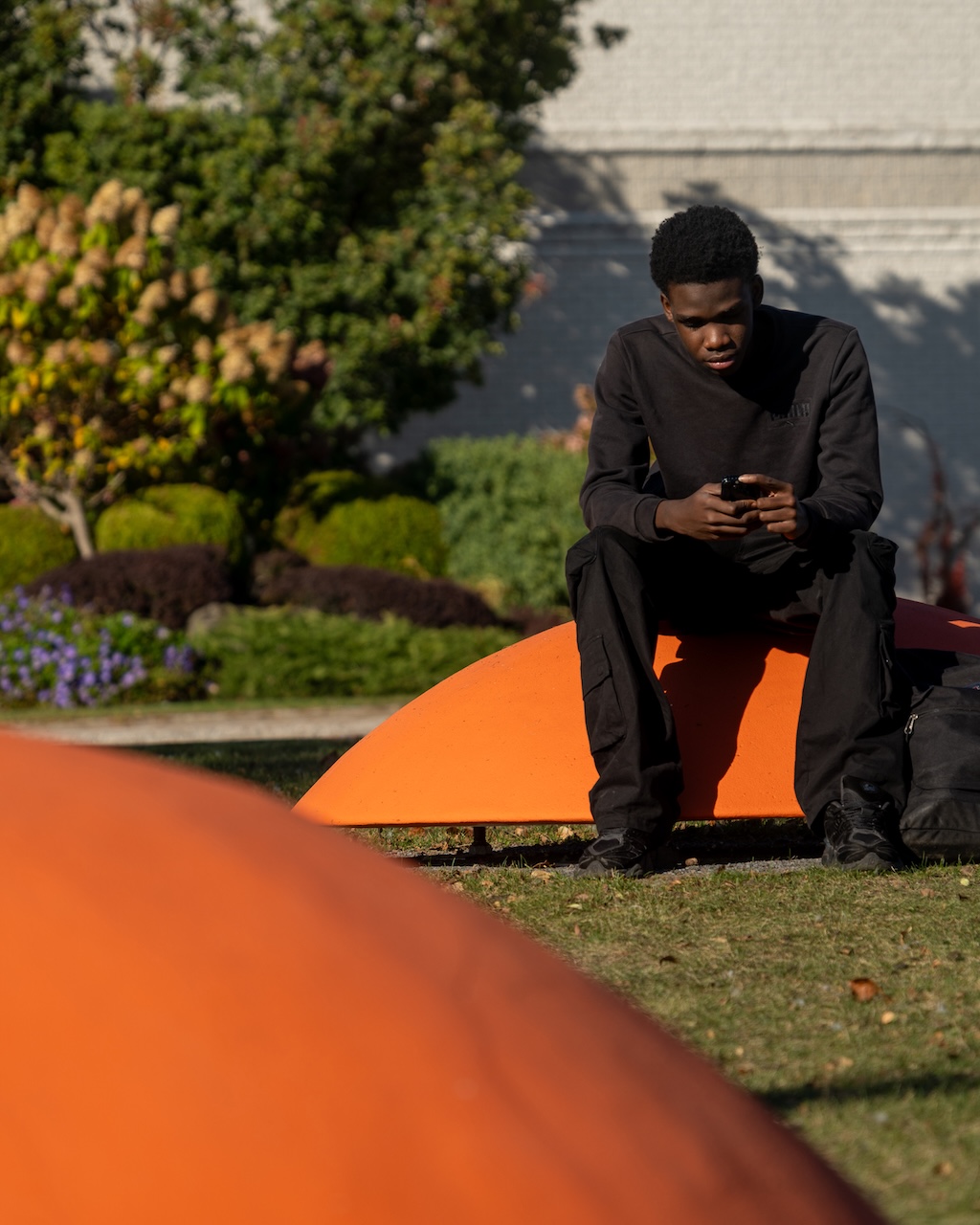 Jeune homme assis sur une installation orange en plein air, regardant son téléphone.