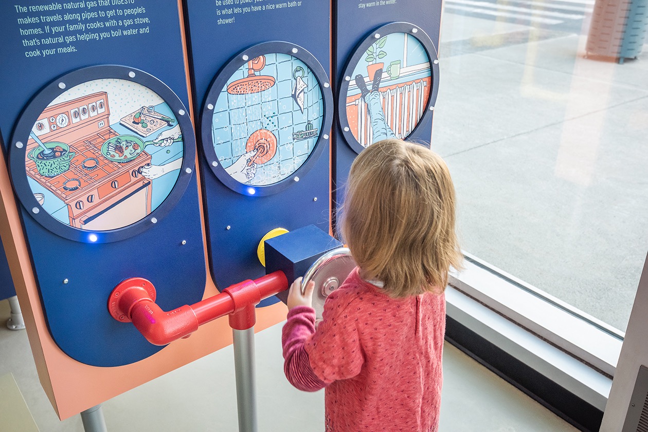 Enfant manipulant une installation interactive sur le gaz naturel dans un musée.