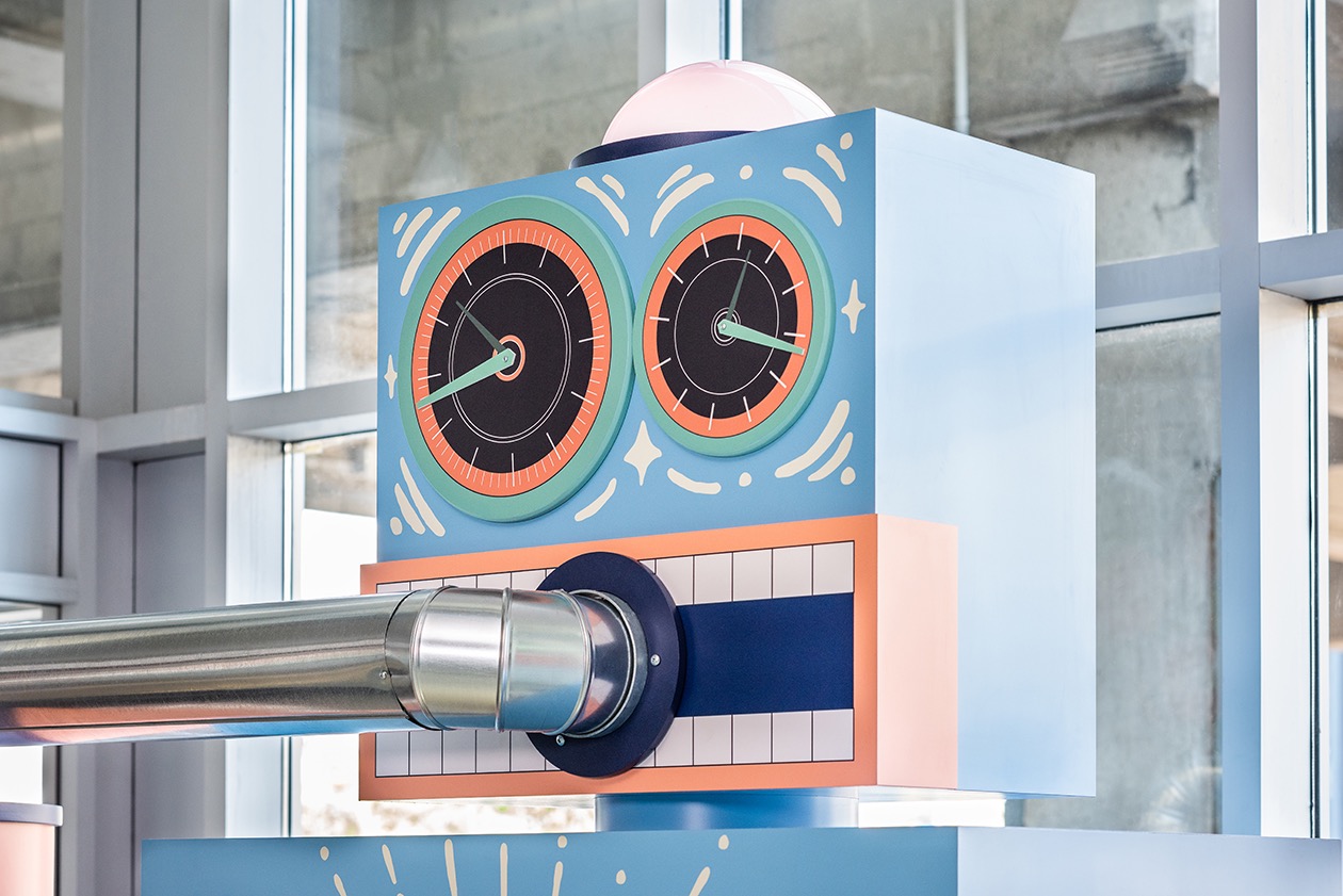 Installation artistique de Studio Overall : horloge stylisée avec deux cadrans et tuyau métallique.