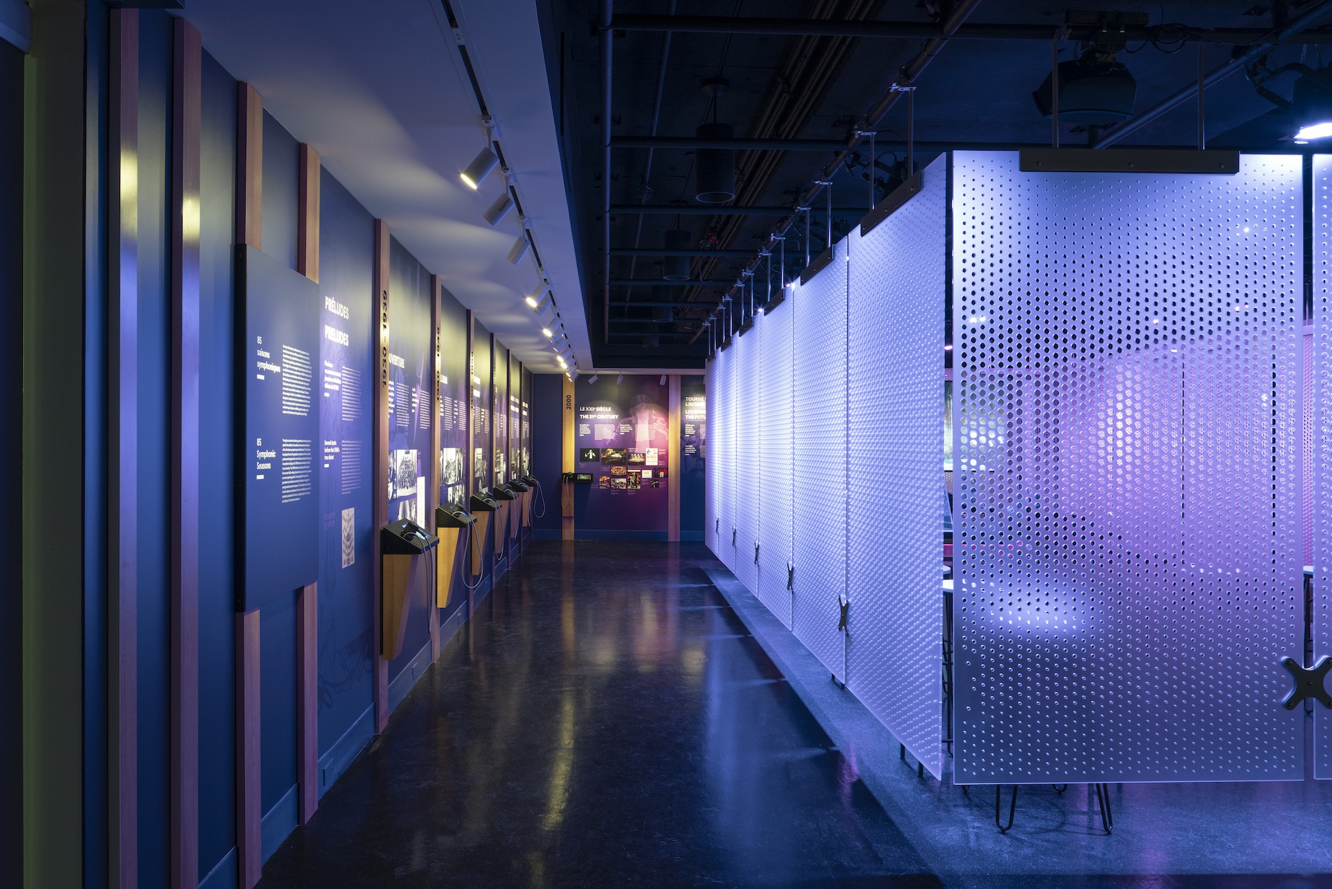 Hall d'exposition avec panneaux perforés lumineux et présentations murales.