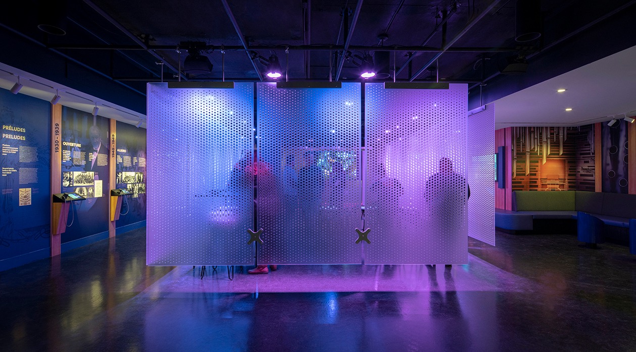 Installation muséographique lumineuse avec visiteurs en arrière-plan, œuvre de Studio Overall.