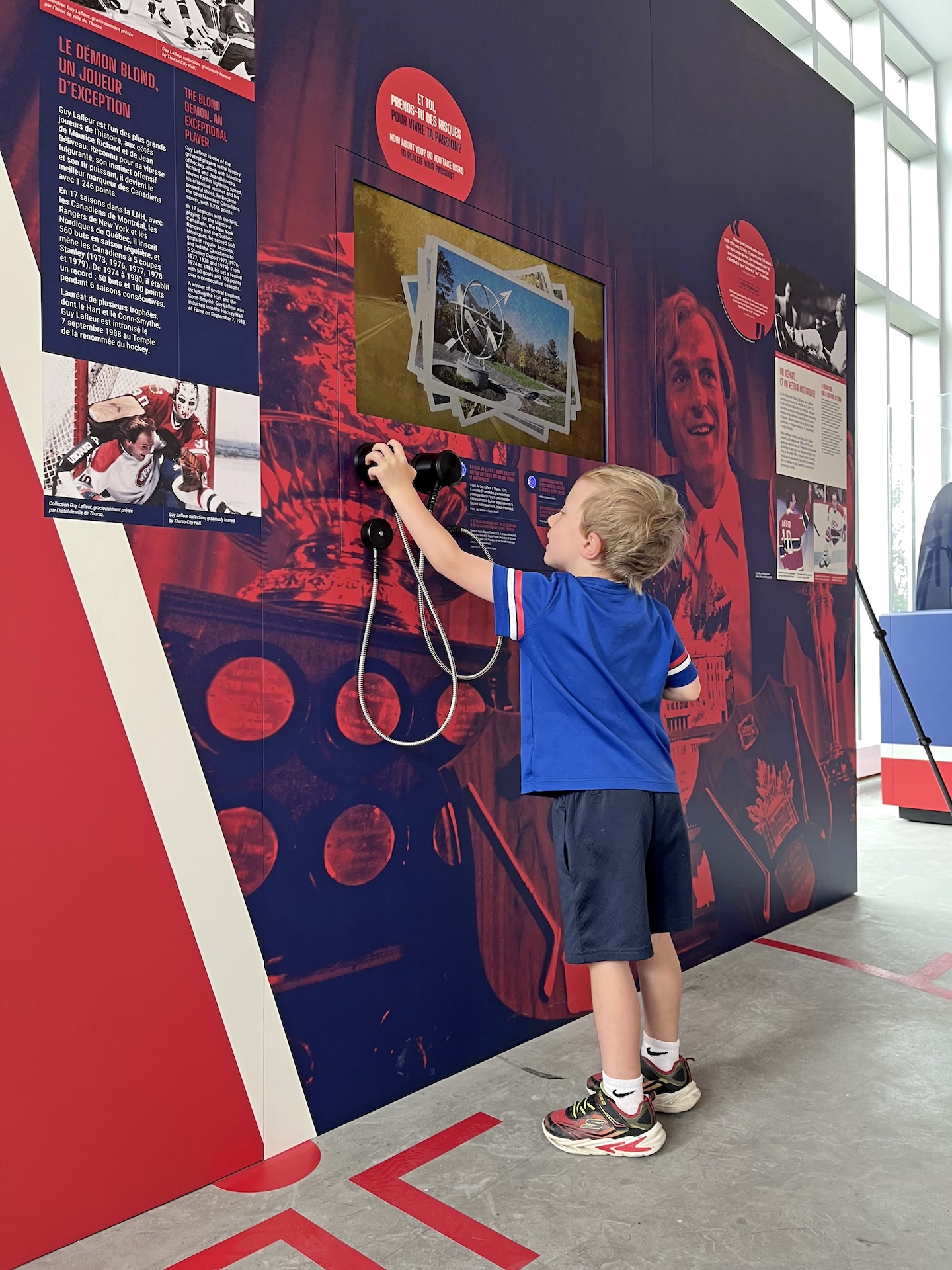Enfant explorant une exposition muséale interactive sur le hockey, avec panneaux bilingues et éléments éducatifs.