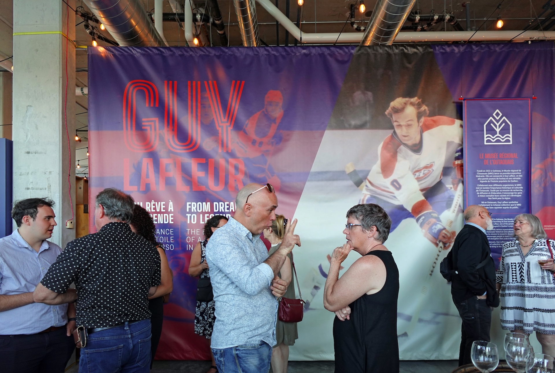 Exposition sur Guy Lafleur au Musée régional de l'Outaouais, visiteurs en discussion devant une grande bannière.