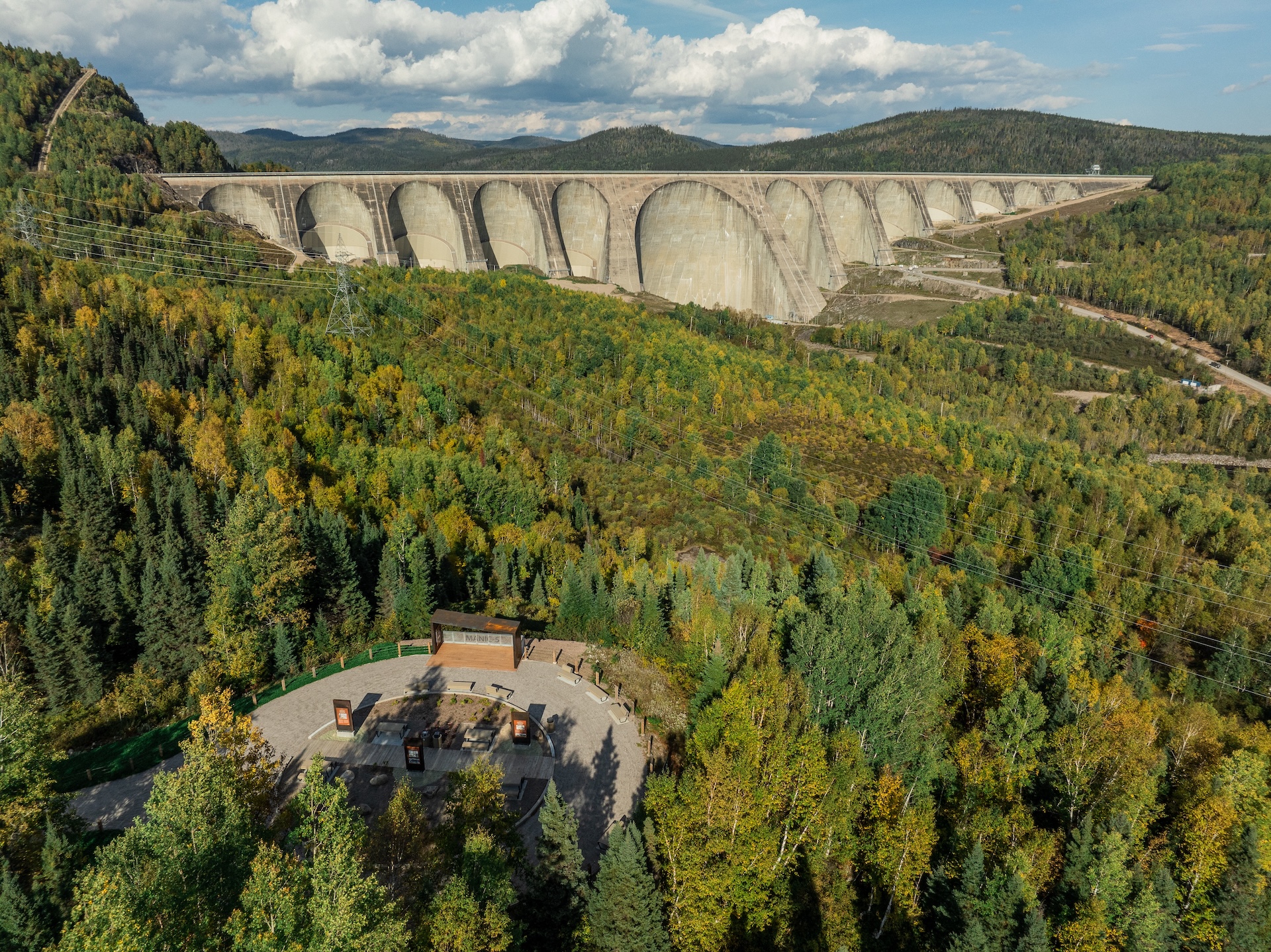 Grand barrage en arc avec forêts colorées en automne, vue aérienne.