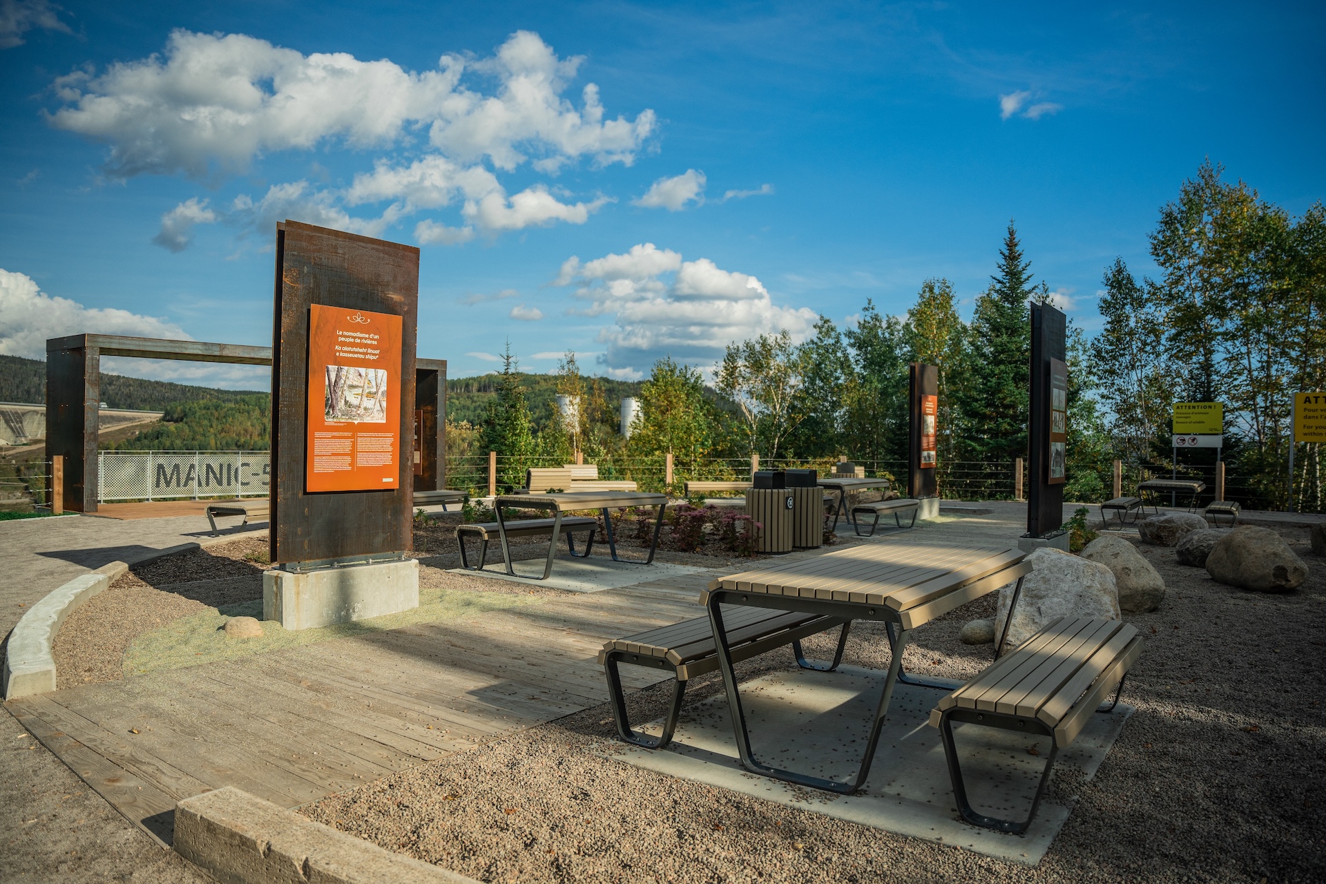 Installation muséographique extérieure de Studio Overall, avec panneaux d'information et bancs en bois.