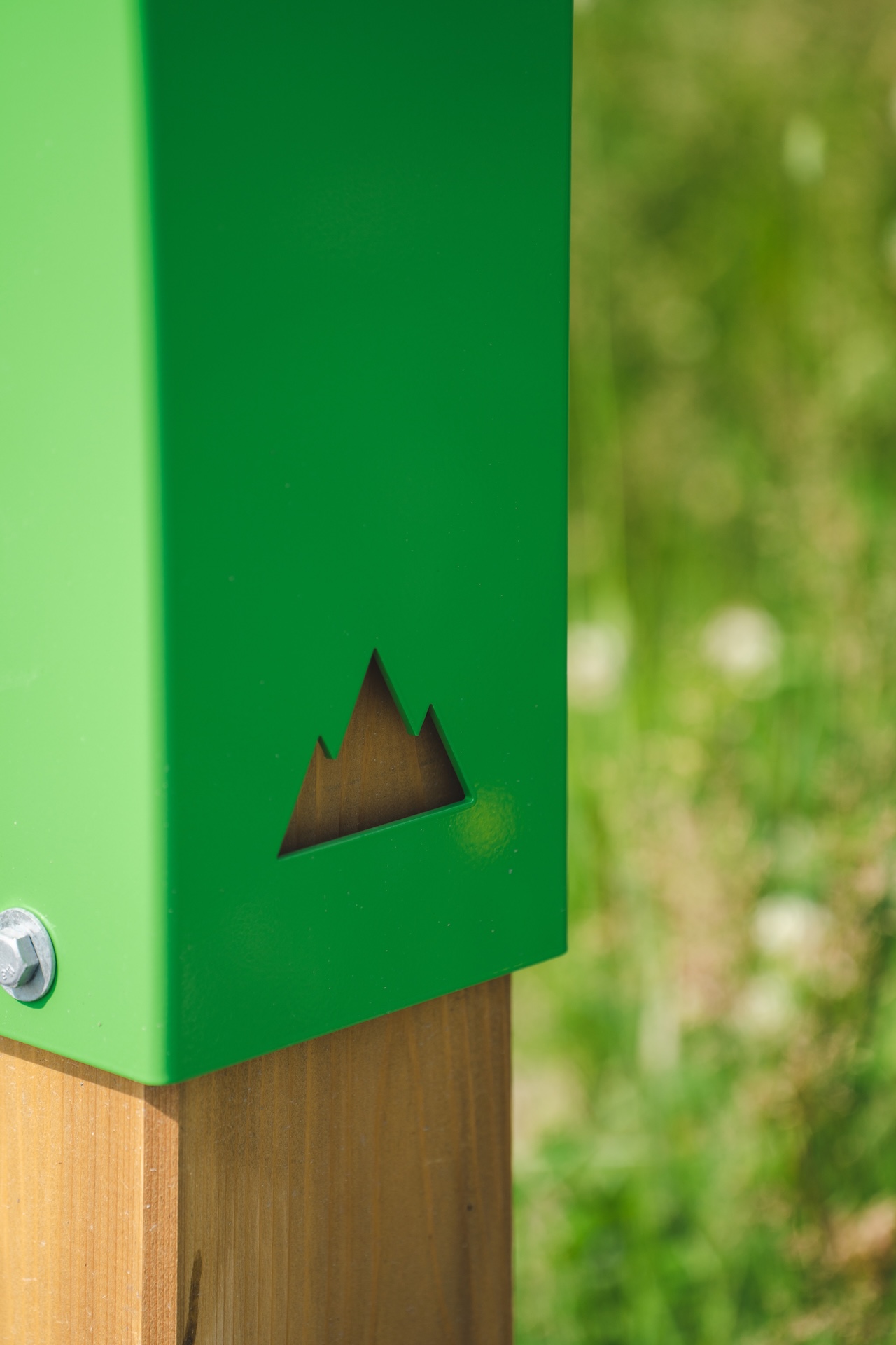 Signalétique verte avec symbole de montagne, installée en extérieur sur un poteau en bois.