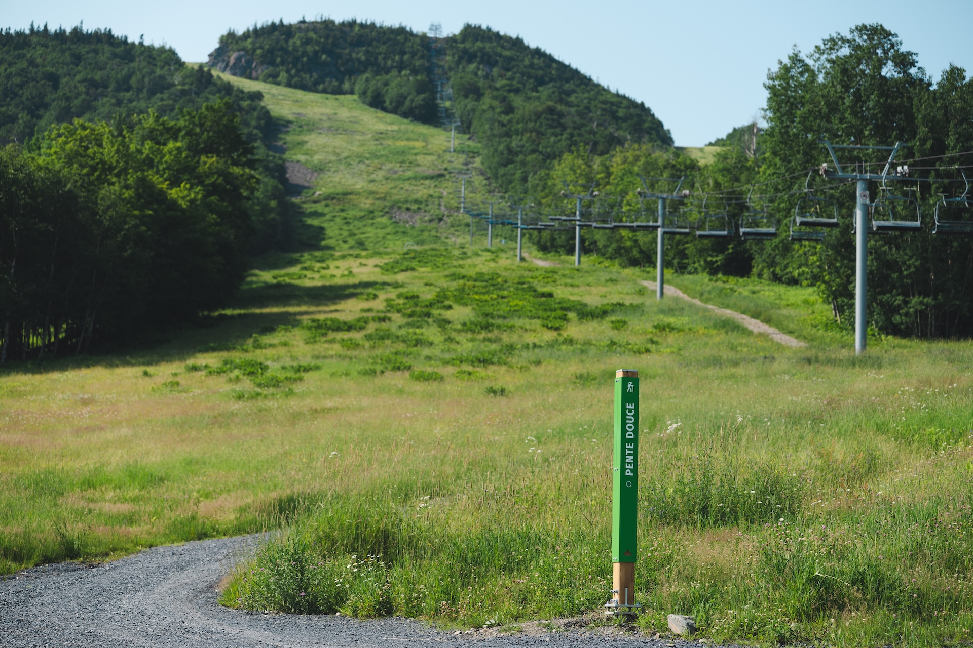 Sentier de randonnée avec pente douce, en bordure d'un téléphérique dans un paysage verdoyant.