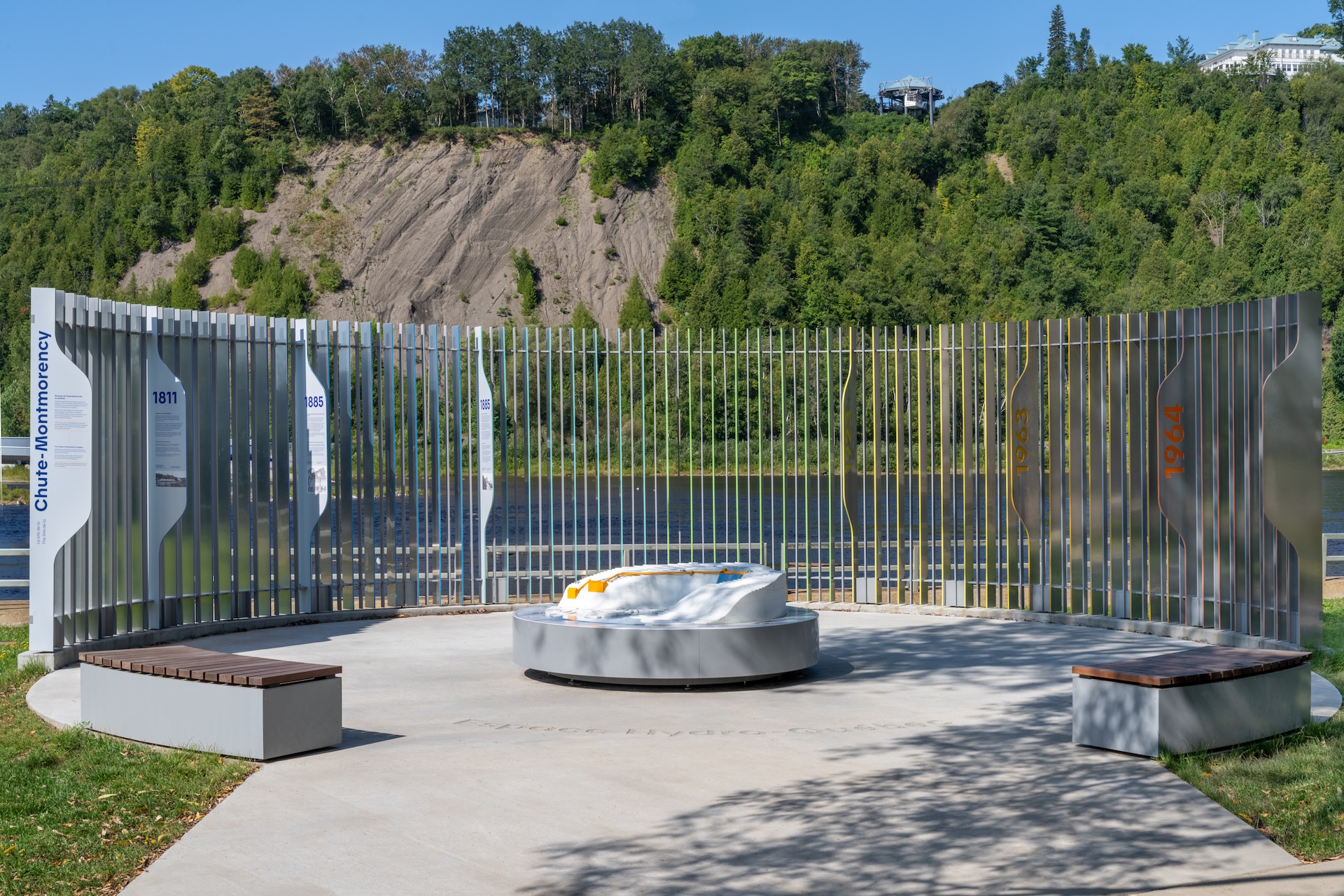Installation muséographique de Studio Overall à la chute Montmorency, avec panneaux historiques et sculpture centrale.