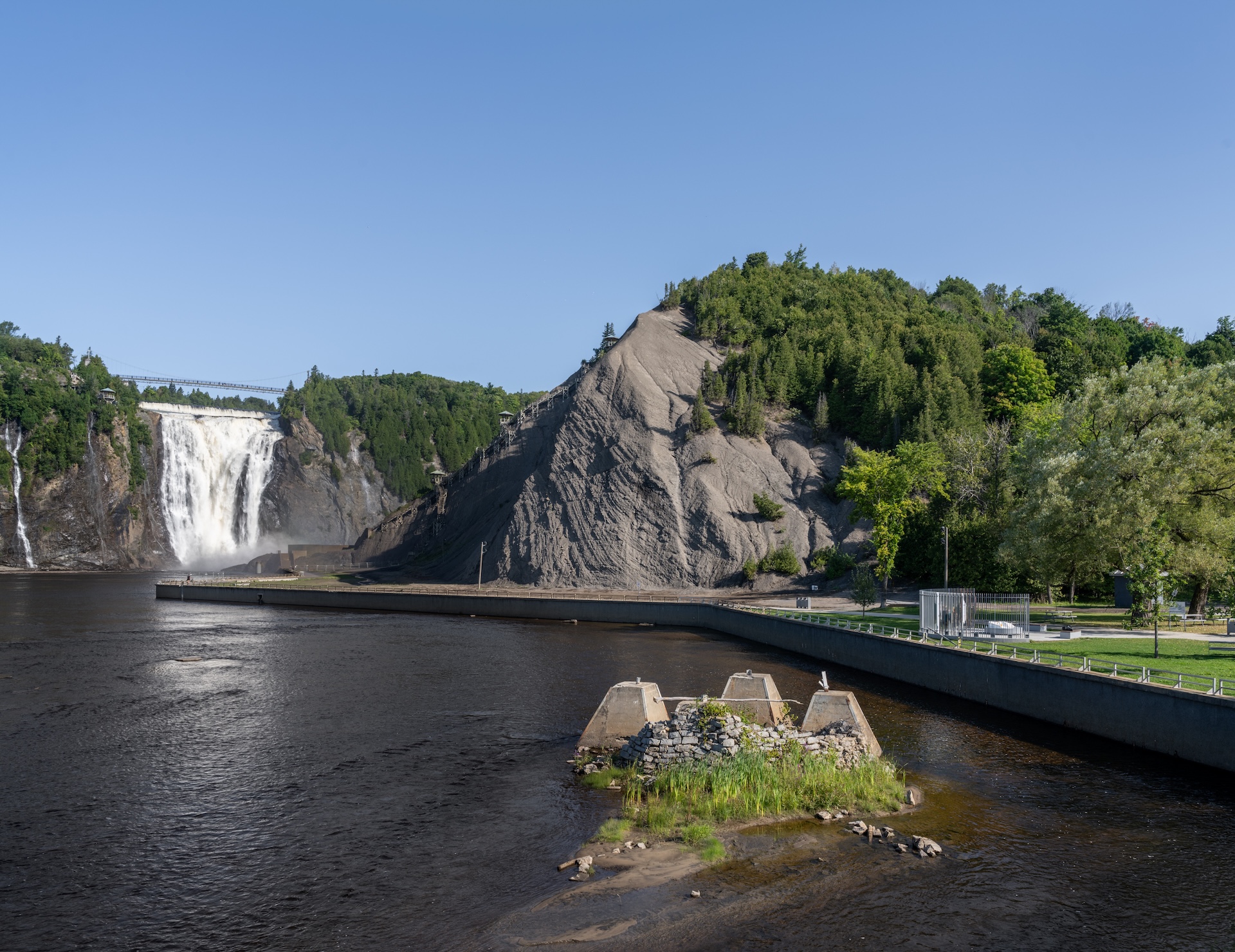 Chute d'eau spectaculaire avec falaise rocheuse et espace vert en bord de rivière.