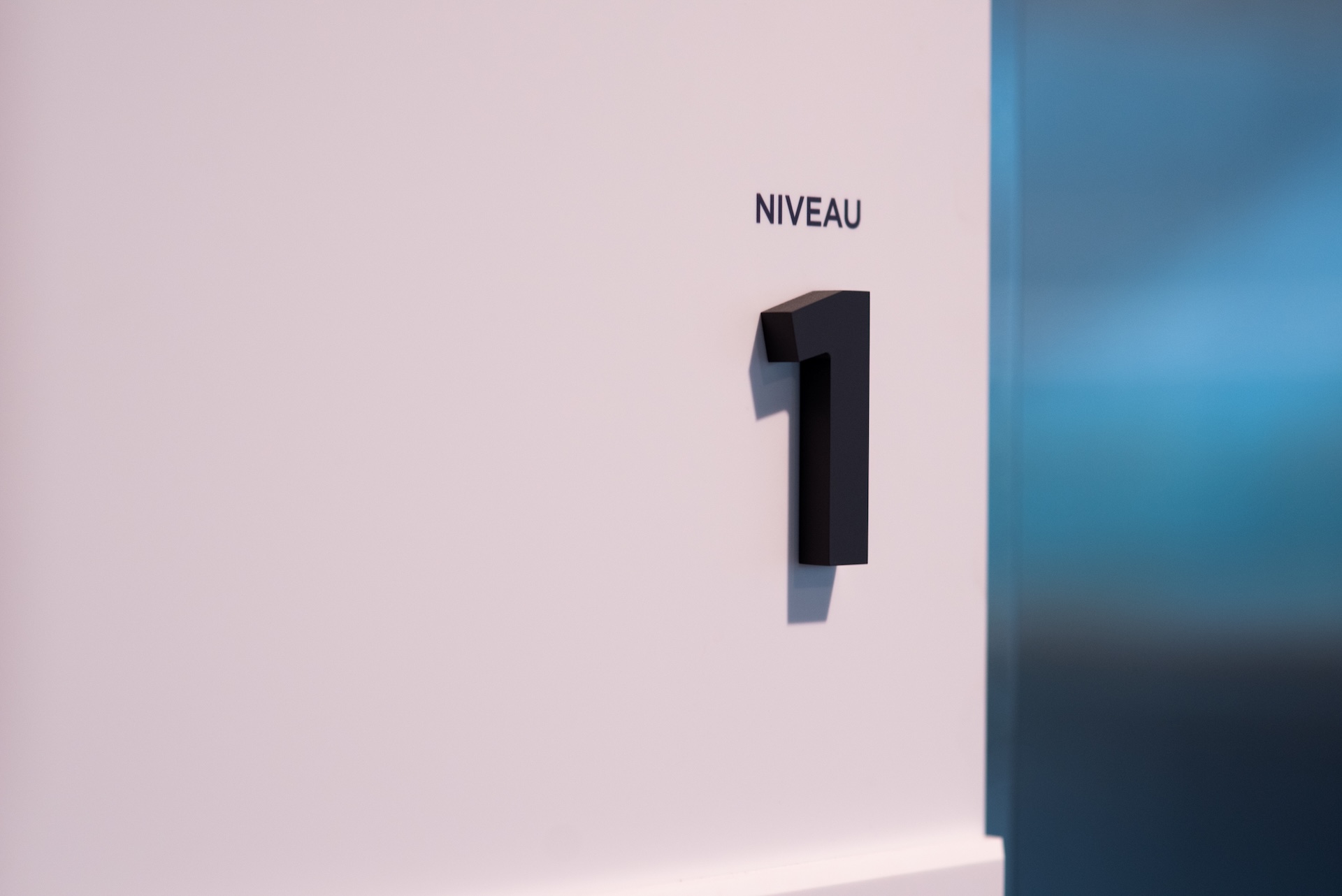 Indication de niveau 1 sur un mur blanc, avec un chiffre noir stylisé, dans un espace moderne.