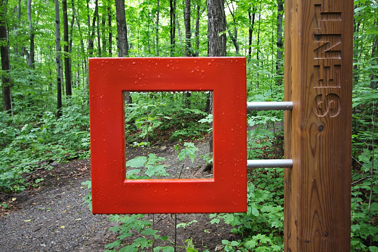 Cadre rouge en forêt, installation de Studio Overall, vue encadrée par un poteau en bois.