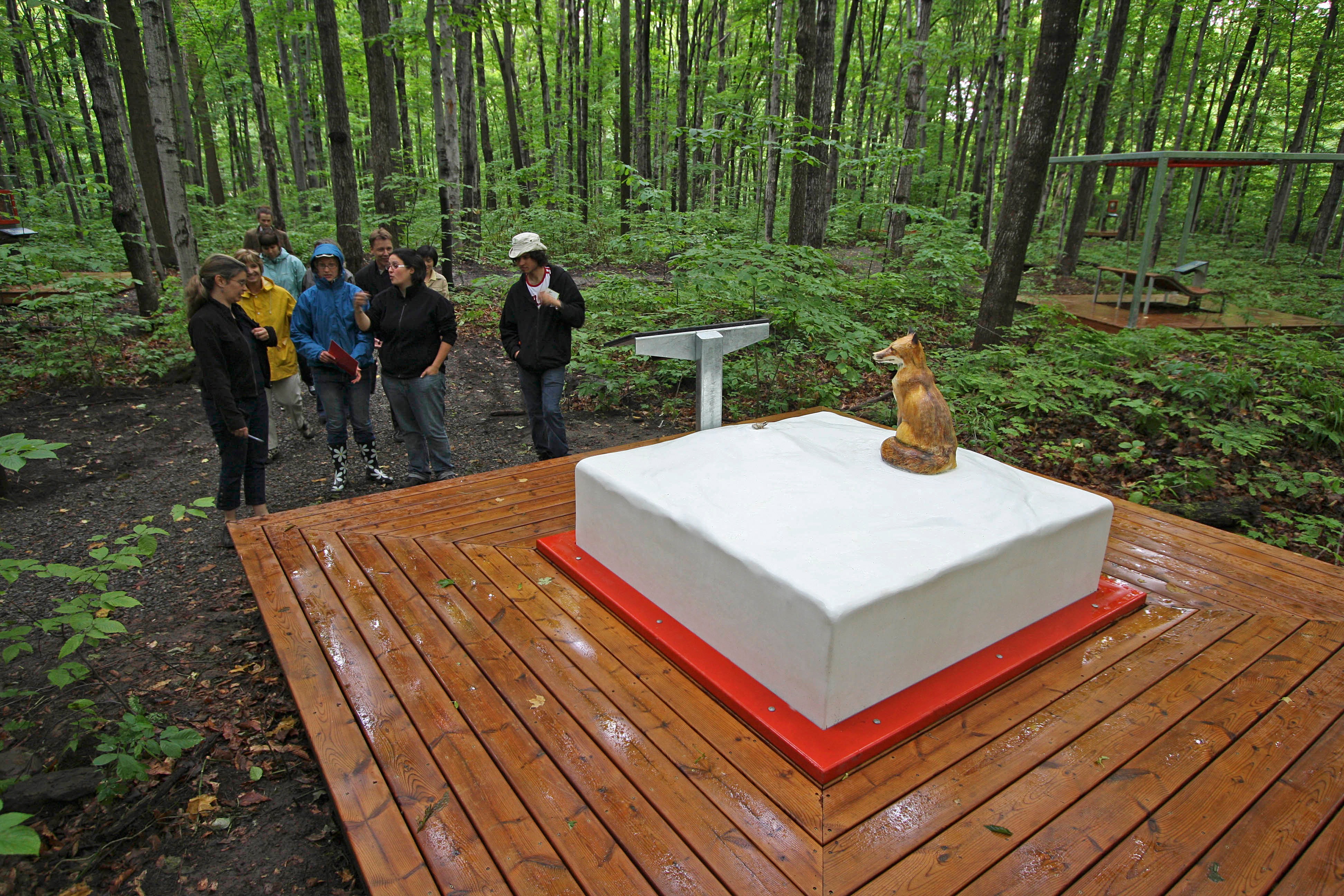 Installation forestière avec statue de renard sur socle blanc, visite guidée en milieu naturel.