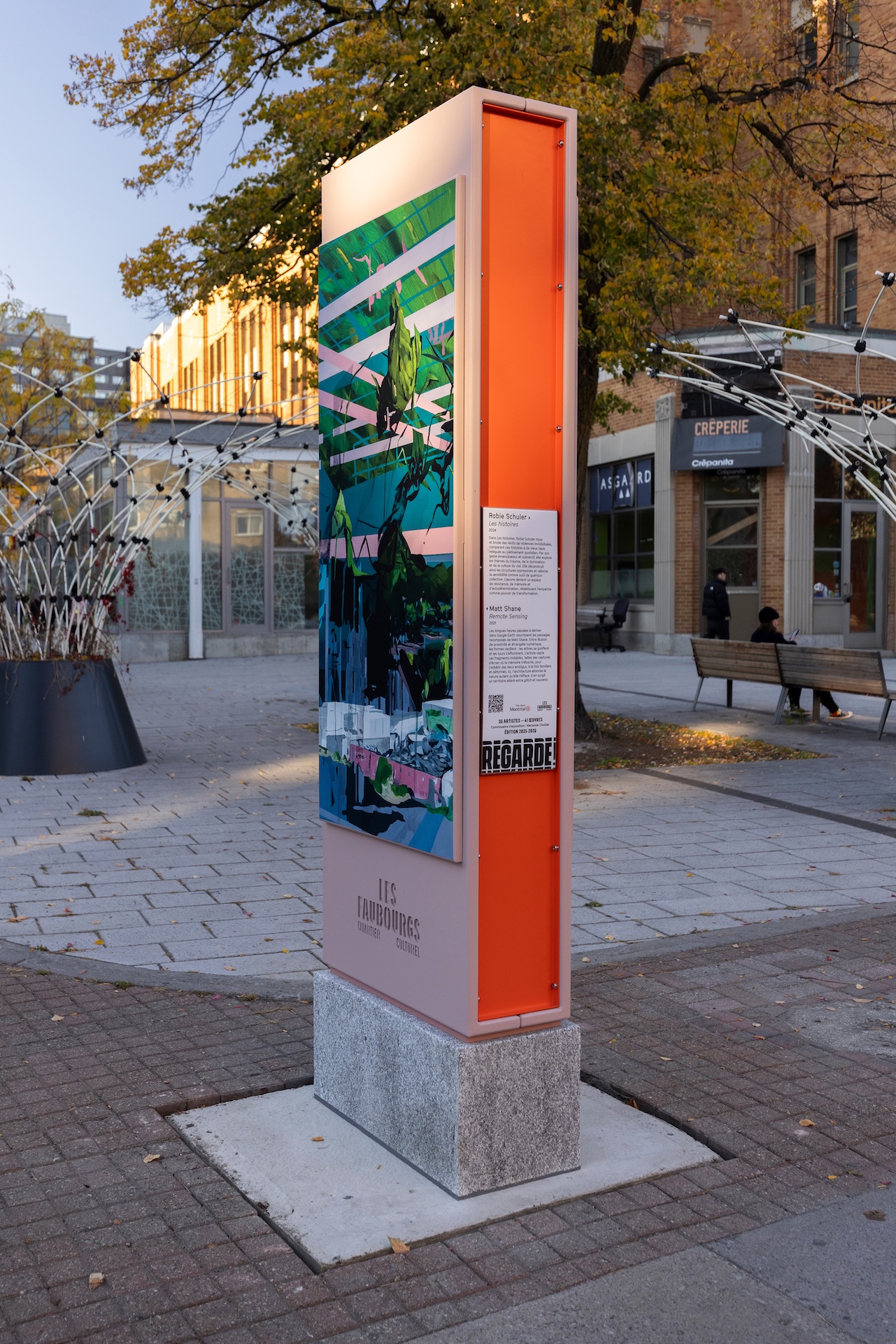 Installation artistique urbaine avec affiche colorée, présentée dans un espace public pavé.