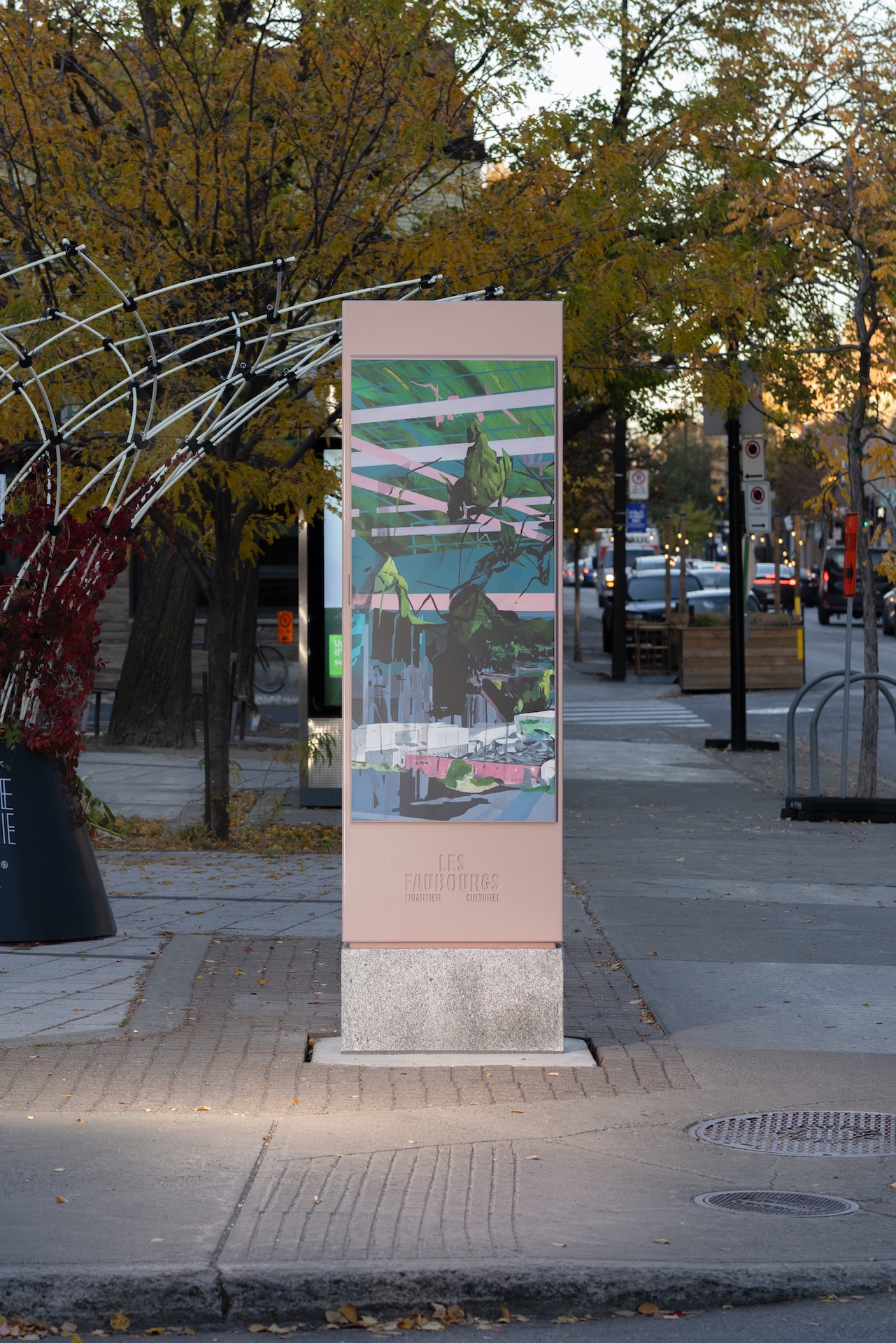 Installation artistique urbaine de Studio Overall, avec affiche colorée et structure métallique dans un quartier bordé d'arbres.